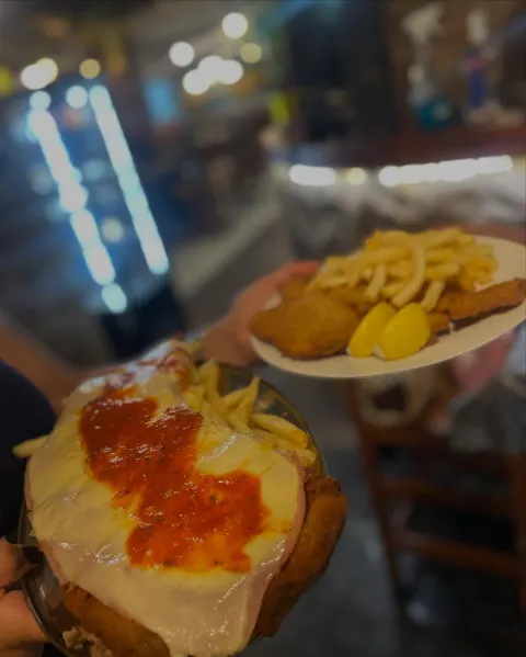 Milanesa napolitana gratinada servida sobre papas fritas