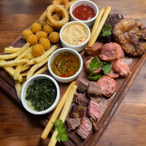 Tabla de picada con cortes de carne, papas, aros de cebolla, croquetas y cuatro salsas