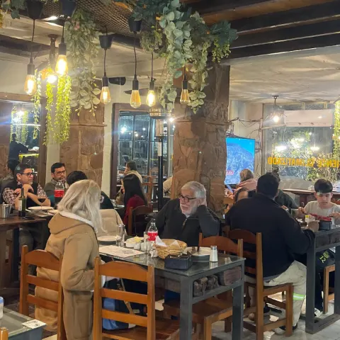Salón lleno de clientes cenando, con plantas colgantes y luces cálidas